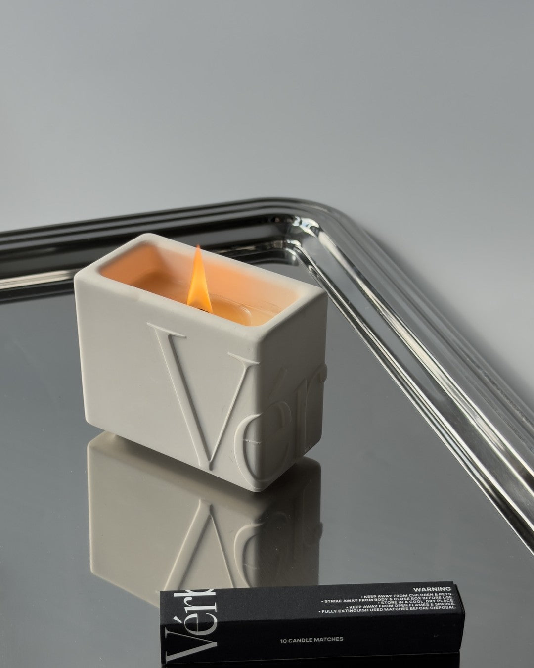 A lit Vérba candle on a mirrored tray
