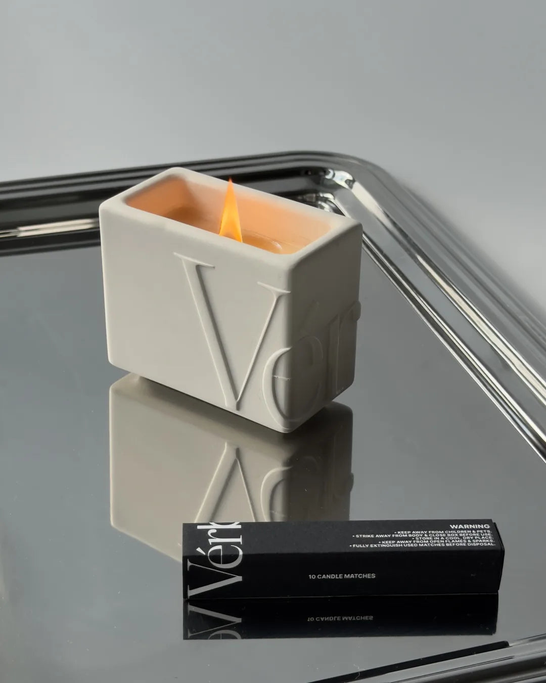 Lit white Vérba candle with a wooden wick on a mirrored tray beside black matches — a luxury candle gift for Diwali