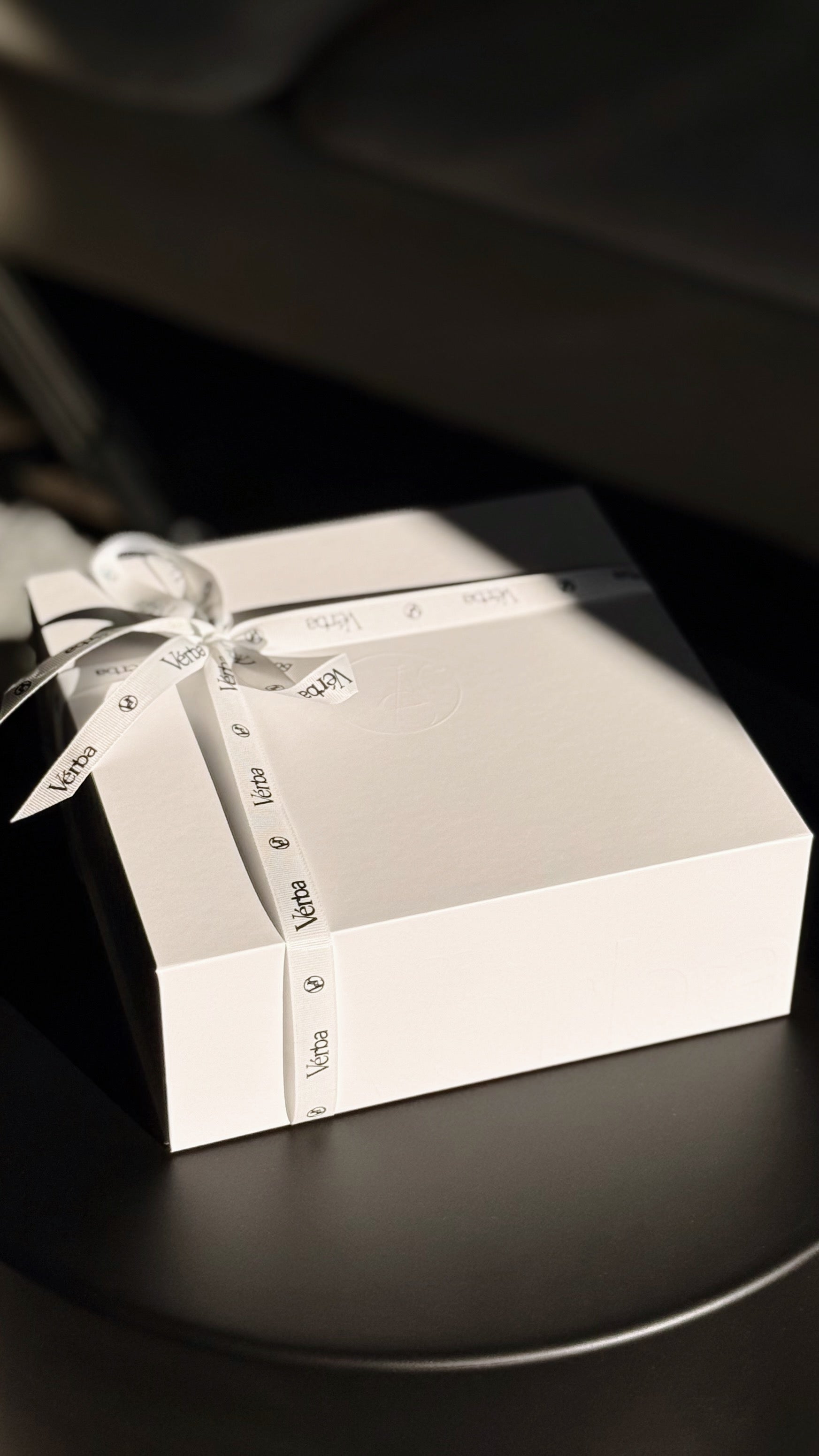 White Verba gift box with a branded ribbon and tag on a dark surface — elegant minimalist packaging.