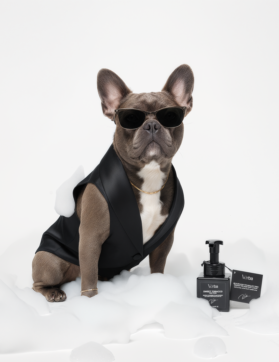 French bulldog wearing black vest and sunglasses sitting beside Verba Sweet Tobacco Perfumed Paw Foam bottle on white background with foam