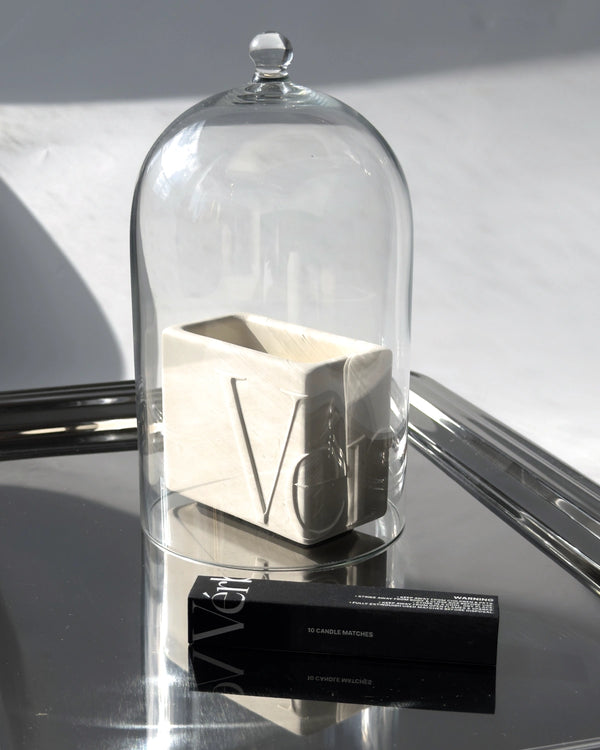 White Vérba candle under a glass cloche on a mirrored tray, holding in its fragrance — fragrance throw